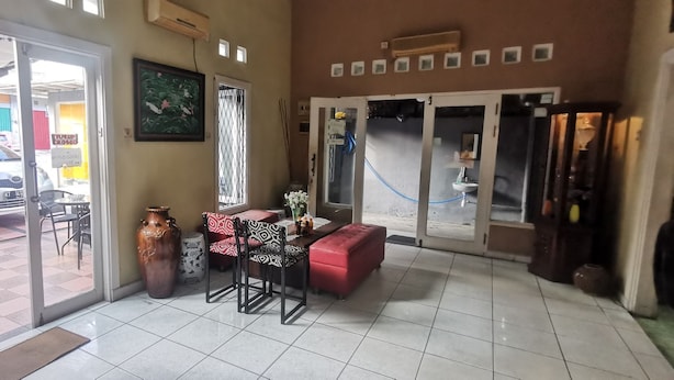 A hotel lobby with a tiled floor, a red sofa, a table with a vase, and a large window with a view of parked cars outside.