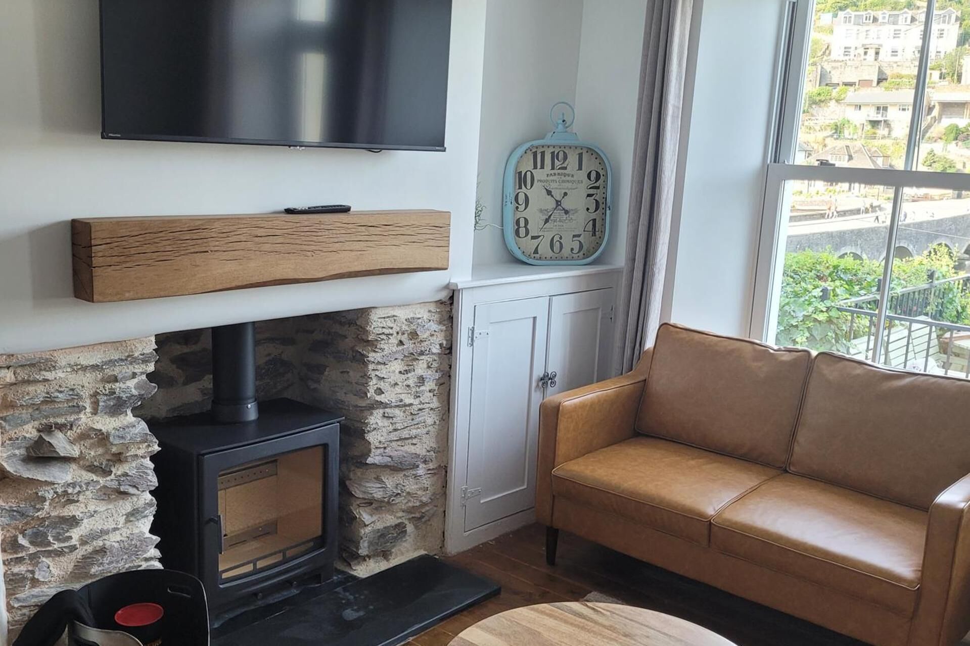 Una sala de estar con chimenea de piedra, televisor montado en la pared, un reloj y un sofá.