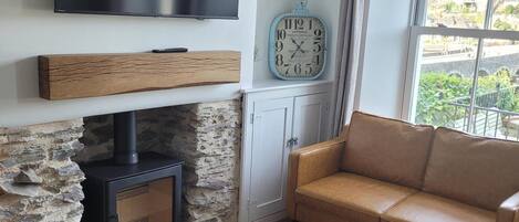 A living room with a stone fireplace, a television mounted on the wall, a clock, and a sofa.