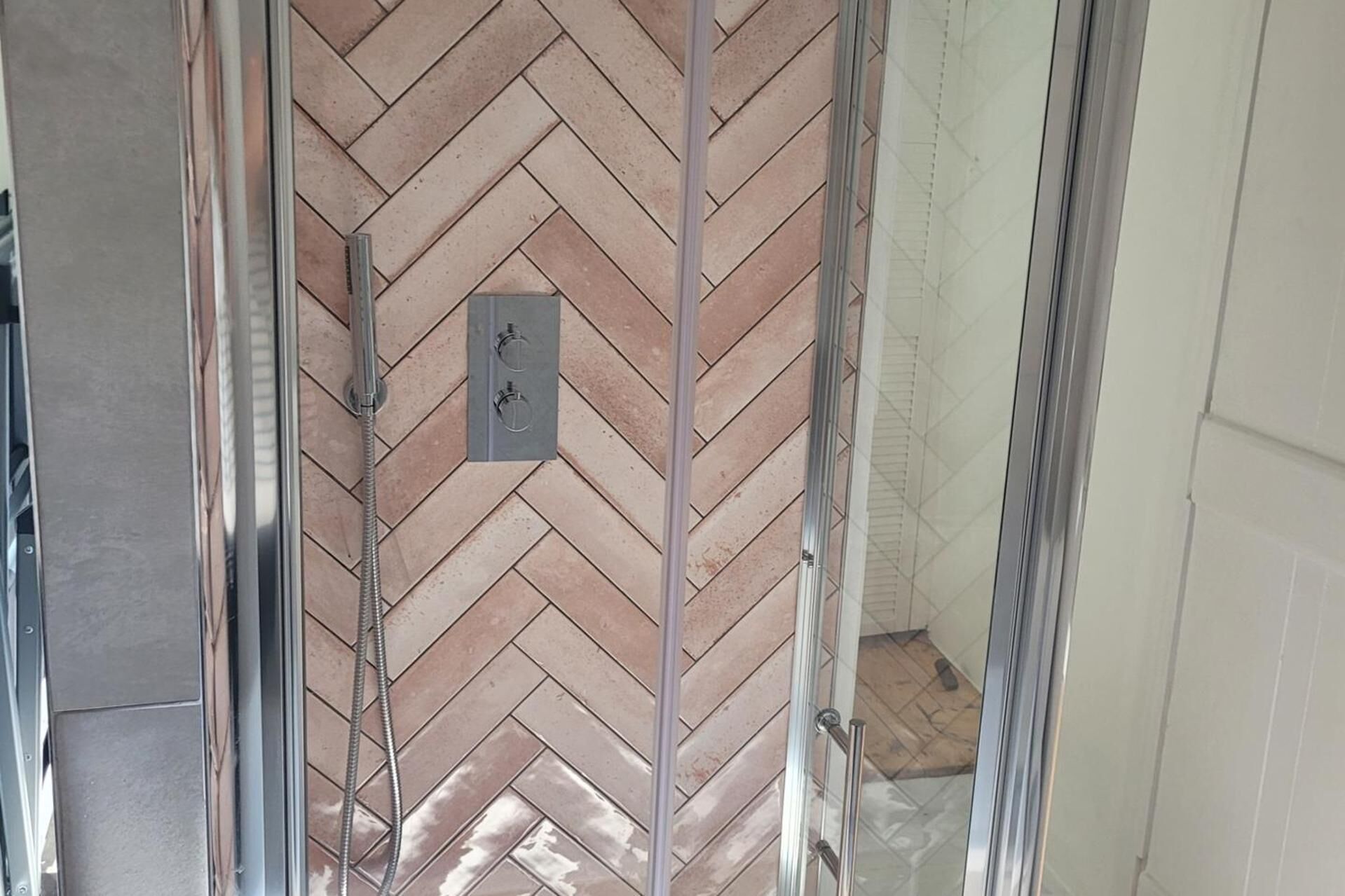 A shower with a herringbone tile pattern and a control panel.