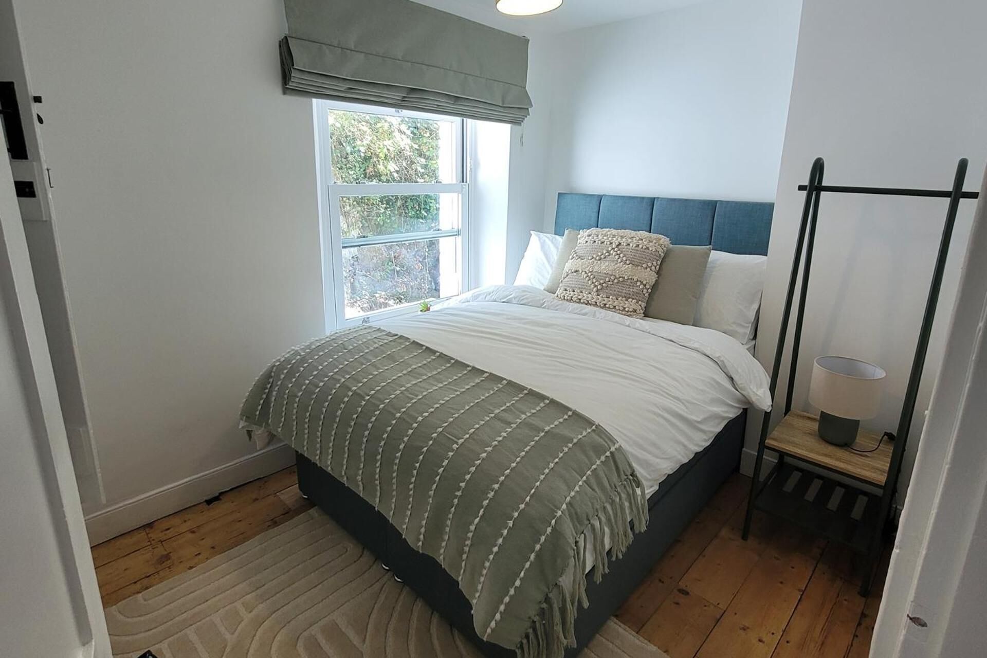 A bedroom with a bed, a window with a view, a bedside table with a lamp, and a headboard.