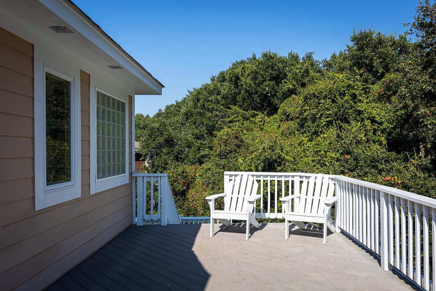 Une terrasse couverte avec deux chaises Adirondack blanches, une balustrade blanche et une vue sur une forêt verdoyante et dense.