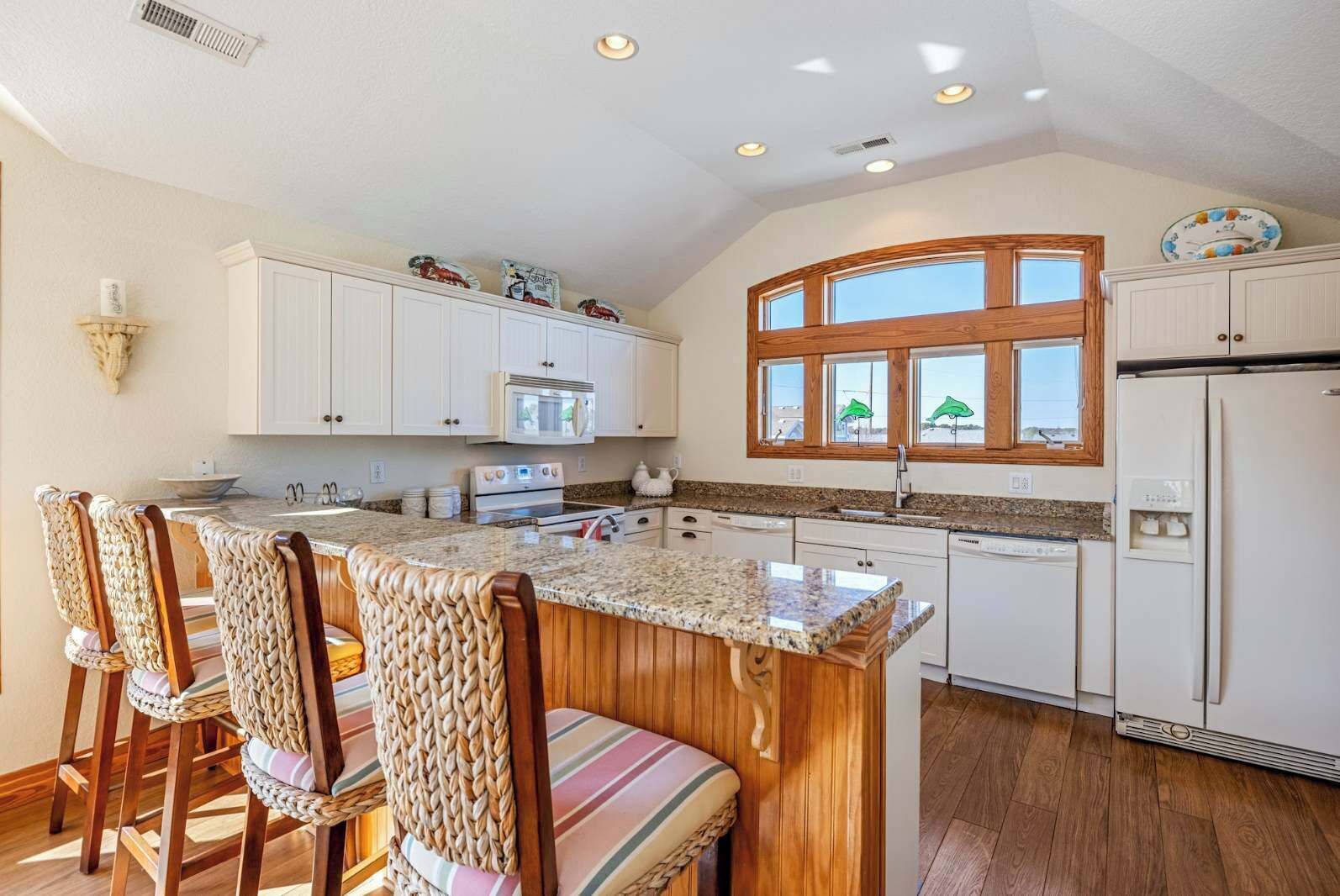 A kitchen with white cabinets, a granite countertop, and a wooden island with chairs.