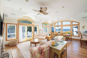 A spacious living room with a large window, a ceiling fan, and a dining area with wooden furniture. - New Listing! Game room, Private pool & Hot Tub (Kitty Hawk)