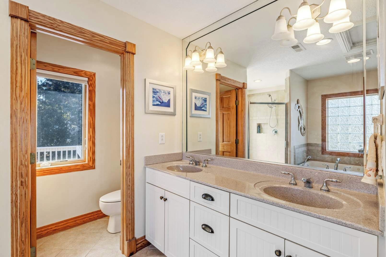 A bathroom with a wooden-framed window, a large mirror, and a double sink with a vanity.