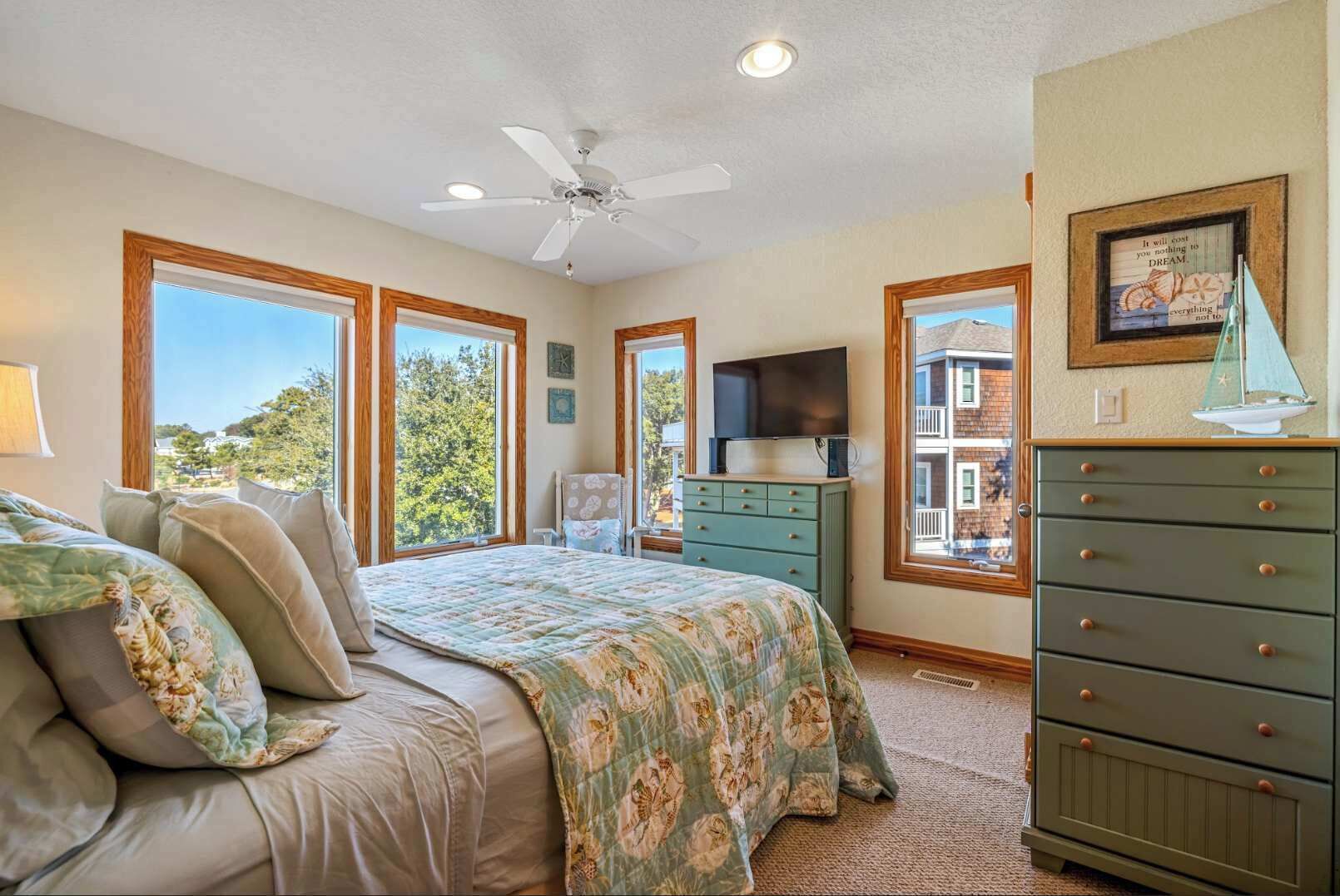 A bedroom with a bed, dresser, TV, and large windows.