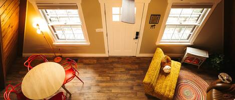 A room with a wooden floor, a ceiling fan, a dining table with red chairs, and a sofa with a colorful rug.