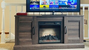 A flat-screen TV mounted on a wooden entertainment center with a fireplace below.