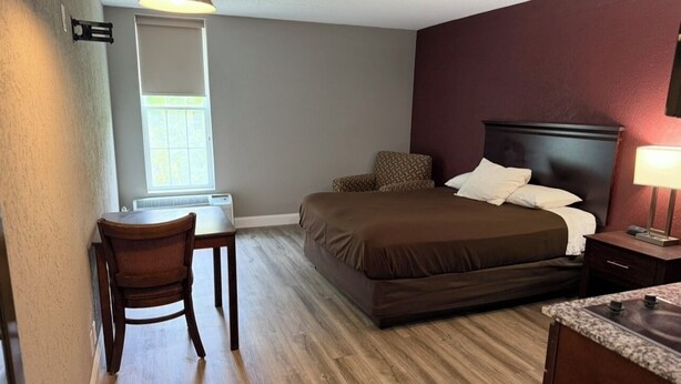 A bedroom with a bed, a desk, a chair, and a nightstand with a lamp. - Fieldstone Apartments & Studios  (Fairmont)