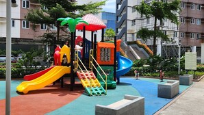 A playground with slides and climbing structures, surrounded by buildings and parked cars. - Colin's Suite at Hope Residences (Trece Martires)