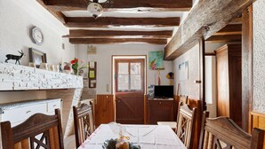 Comedor con mesa dispuesta para cuatro, sillas de madera, un cuenco decorativo con pan y techo rústico.