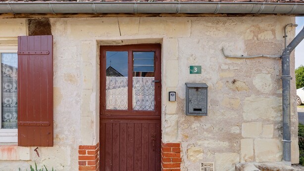 Un edificio de piedra con puerta de madera, un cartel con el número 3 y un cuadro de contadores.