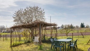 Un espacio de estar al aire libre cubierto con una mesa y sillas, rodeado de un campo de césped y árboles.