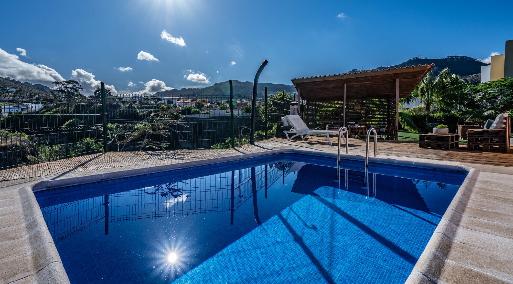 Ein Pool mit Blick auf Berge, eine überdachte Sitzgelegenheit und ein umzäunter Garten.