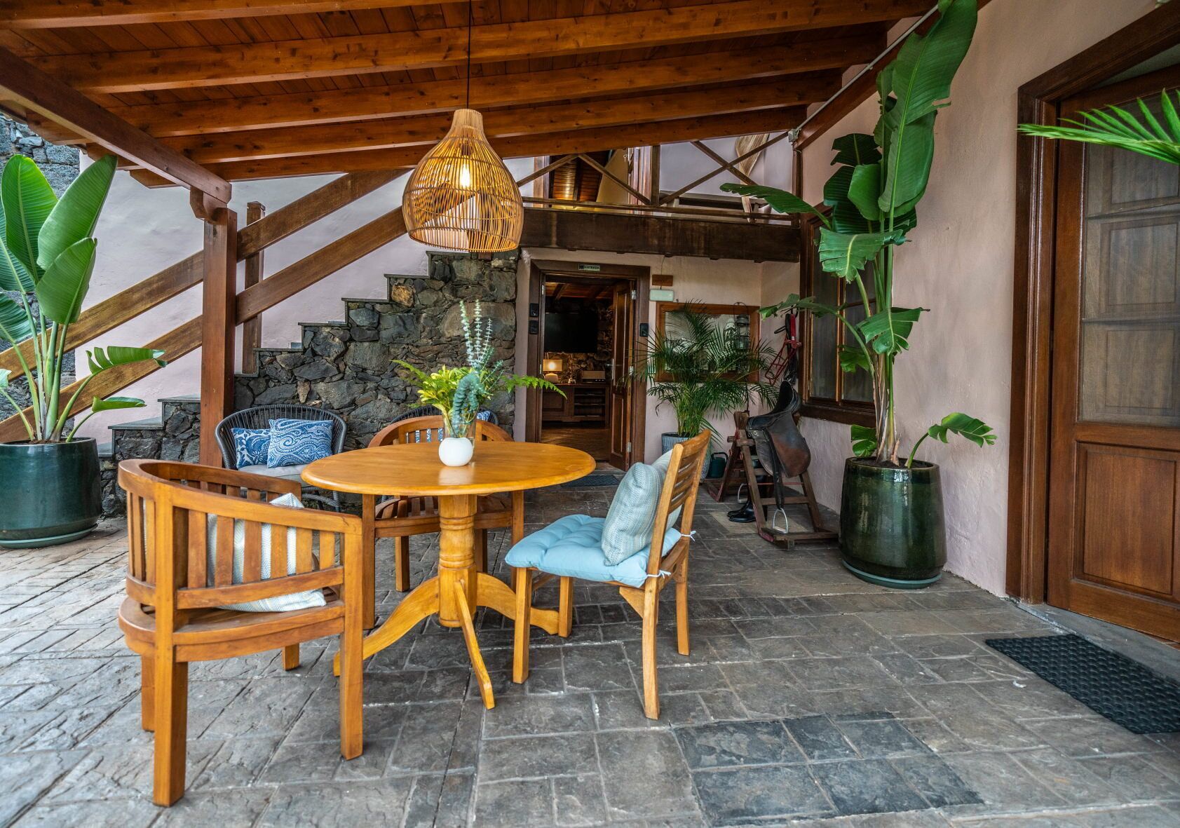 A wooden dining table with chairs, a hanging light fixture, and potted plants.
