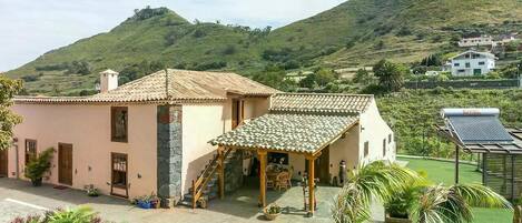 A two-story building with a tiled roof, a covered patio, and a garden area with potted plants.