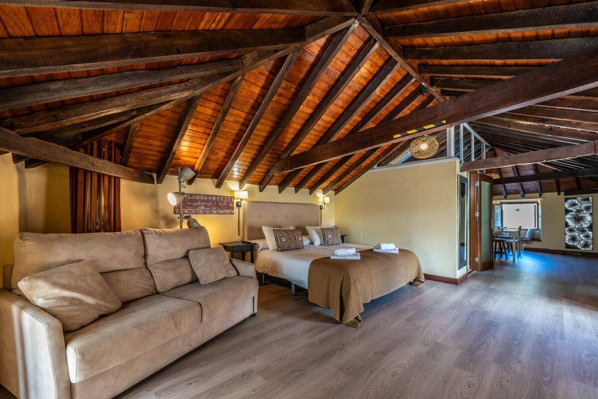 A spacious room with a high wooden ceiling, a sofa, a bed, and a dining area.