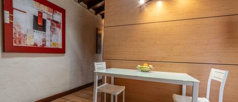 Un comedor con pared de madera, una mesa blanca, dos sillas blancas y un frutero sobre la mesa.