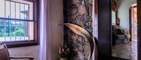 A room with a stone wall, a wooden bench, a potted plant, and a view through a window.