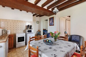 A kitchen with a dining table, chairs, a microwave, an oven, and a wooden ceiling.