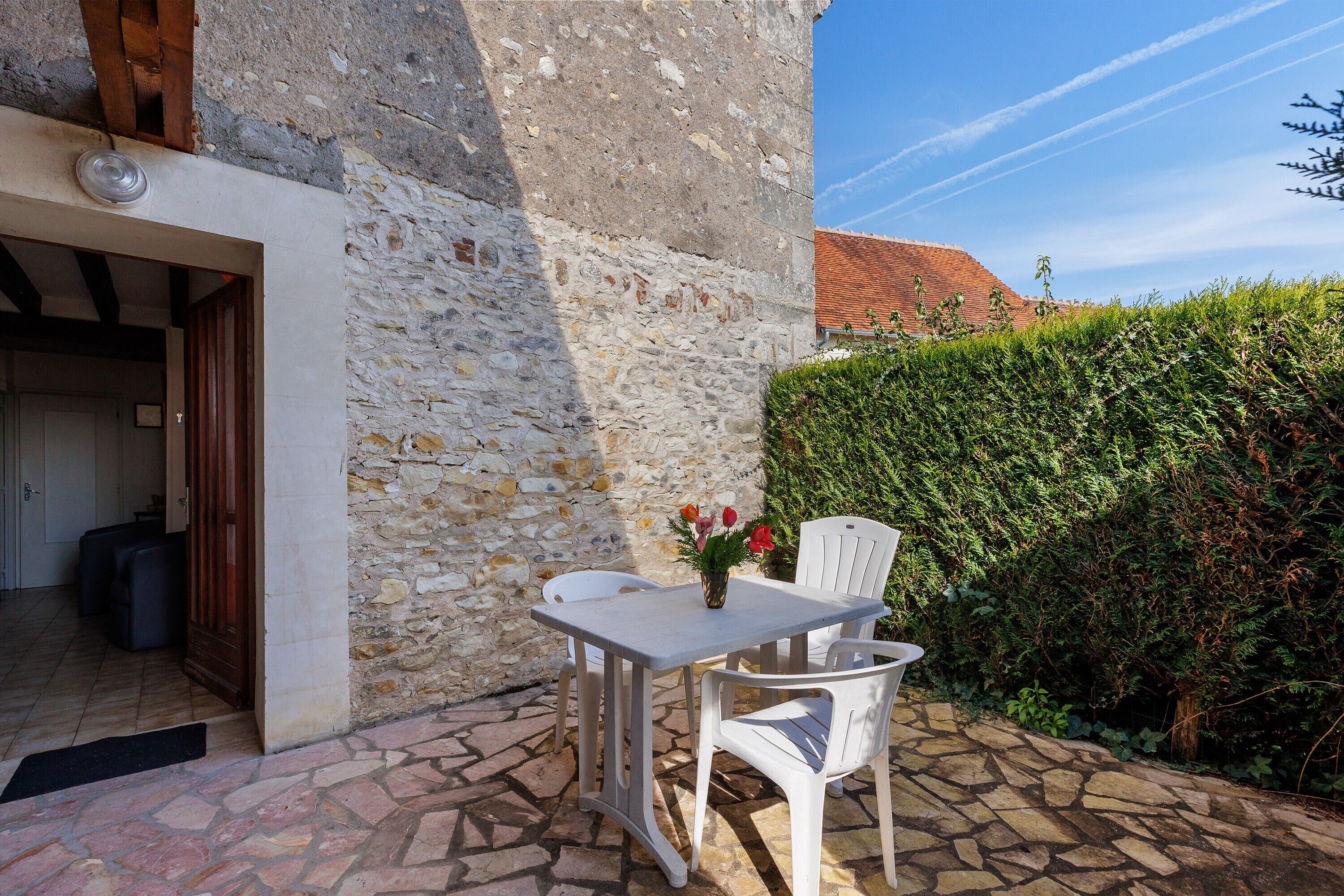 A stone building with a white door, a small table with chairs, and a potted plant with flowers.