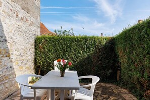 A stone wall, a white table with chairs, and a hedge in a garden setting.