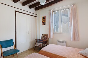 A bedroom with a bed, a chair, a window with curtains, a radiator, and a door.