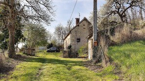 Ein Gebäude aus Stein mit einem geneigten Dach, umgeben von Bäumen und Gras.