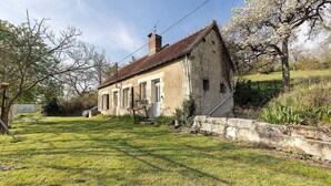 Ein rustikales Steinhaus mit geneigtem Dach, einer kleinen Veranda und einem gepflegten Rasen.