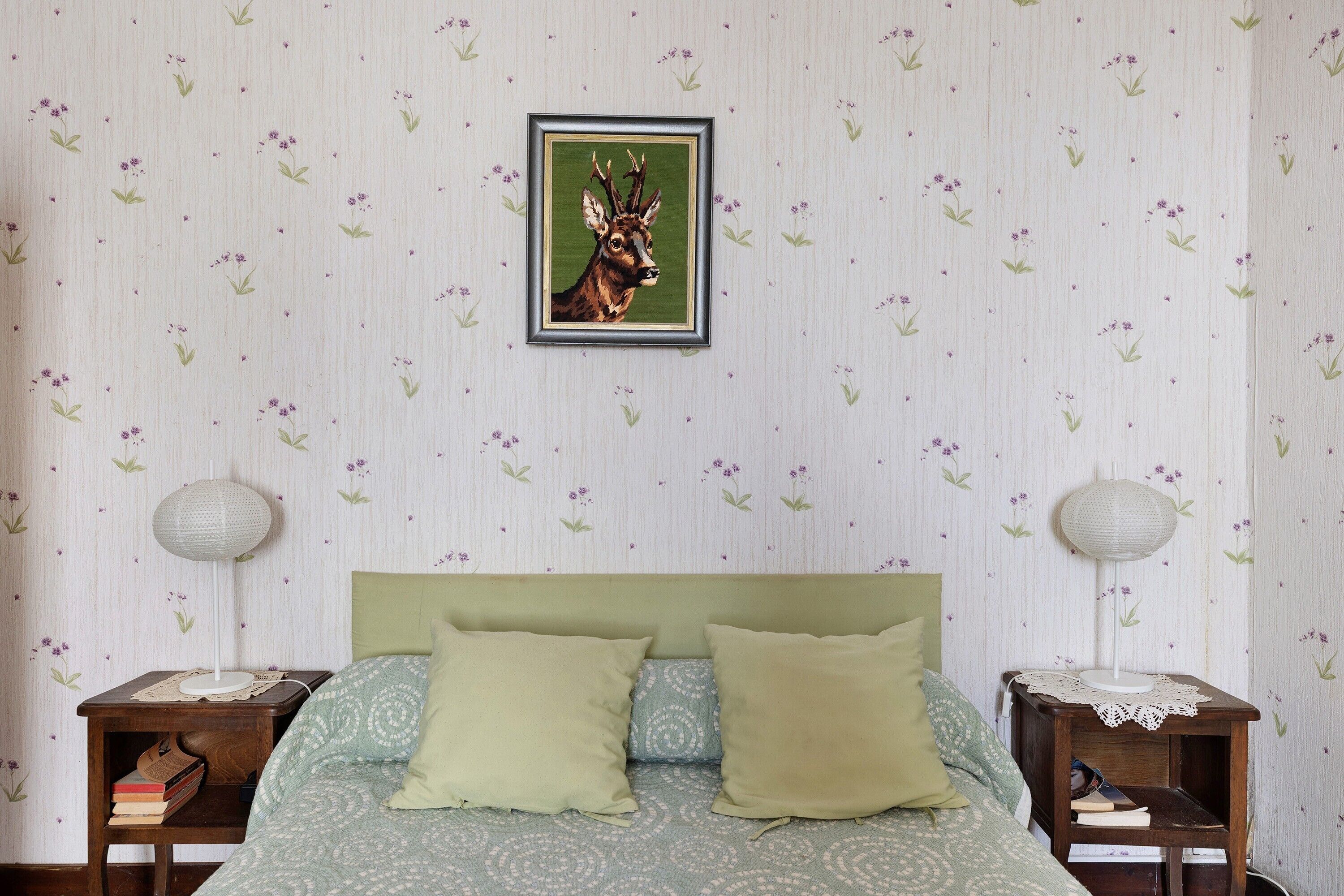Un dormitorio con una cama, dos mesitas de noche, un cuadro enmarco y un papel tapiz estampado.