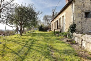 A grassy courtyard with a stone wall, a tree, and a building with arched windows.