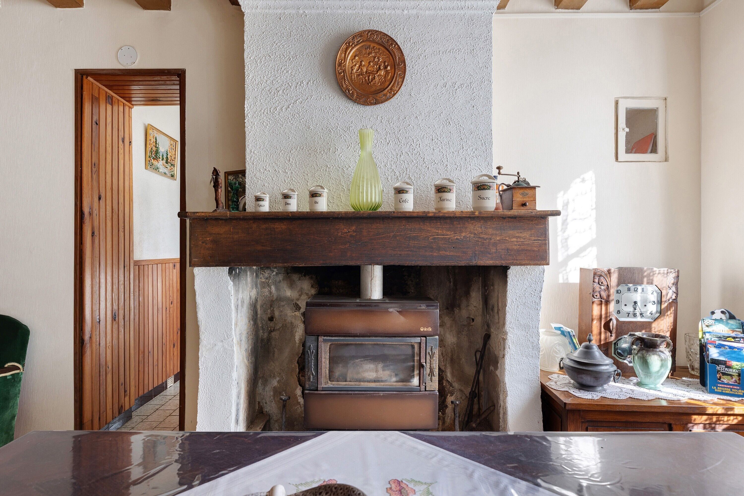 A rustic kitchen with a wood-burning stove, a green vase on the mantel, and a wooden door leading to another room.