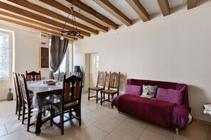 A dining area with a wooden table and chairs, a red sofa, and a ceiling with exposed beams.