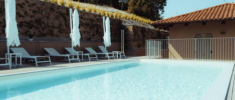 A swimming pool with lounge chairs and umbrellas, a tiled roof, and a wall with climbing plants.