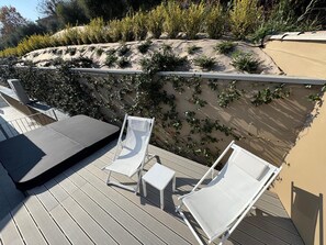 Una terraza con dos sillones blancos, una pequeña mesa y un sofá de color oscuro.