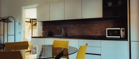 A modern kitchen with a glass dining table, yellow chairs, white cabinets, and a microwave.