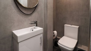 A modern bathroom with a round mirror, white sink, and toilet. - Apartment 9 (York)