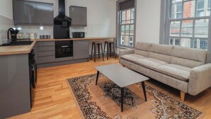 A modern kitchen with a central island, a grey sofa, and a patterned rug. - Apartment 9 (York)