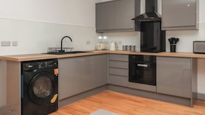 A modern kitchen with grey cabinets, a black washing machine, and a built-in oven. - Apartment 9 (York)