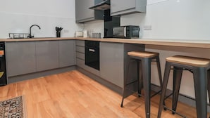 A modern kitchen with grey cabinets, a black oven, a coffee maker, and two stools. - Apartment 9 (York)
