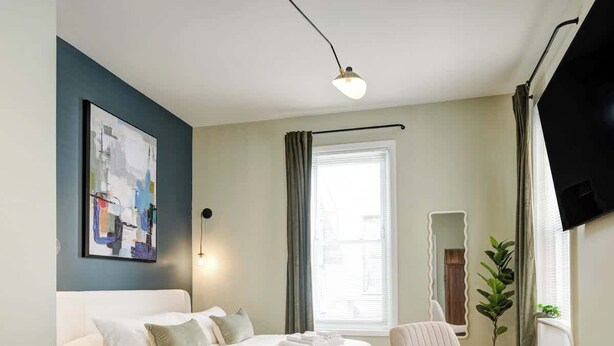 Ein modernes Schlafzimmer mit Bett, Sessel, Schreibtisch, Fernseher und Fenster.