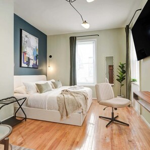 A modern bedroom with a bed, a chair, a desk, a TV, and a window. - Charming Studio w/ King Bed in Washington Square (Philadelphia)
