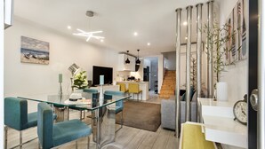 A modern living room with a glass dining table, teal chairs, a sofa, and a kitchen in the background. - Casa dos Quatro in Faro (Faro)