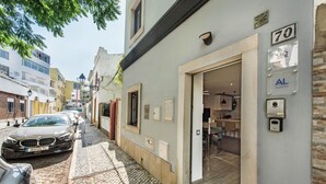 A cobblestone street with parked cars, a building with a number '70' sign, and a visible entrance to a property. - Casa dos Quatro in Faro (Faro)