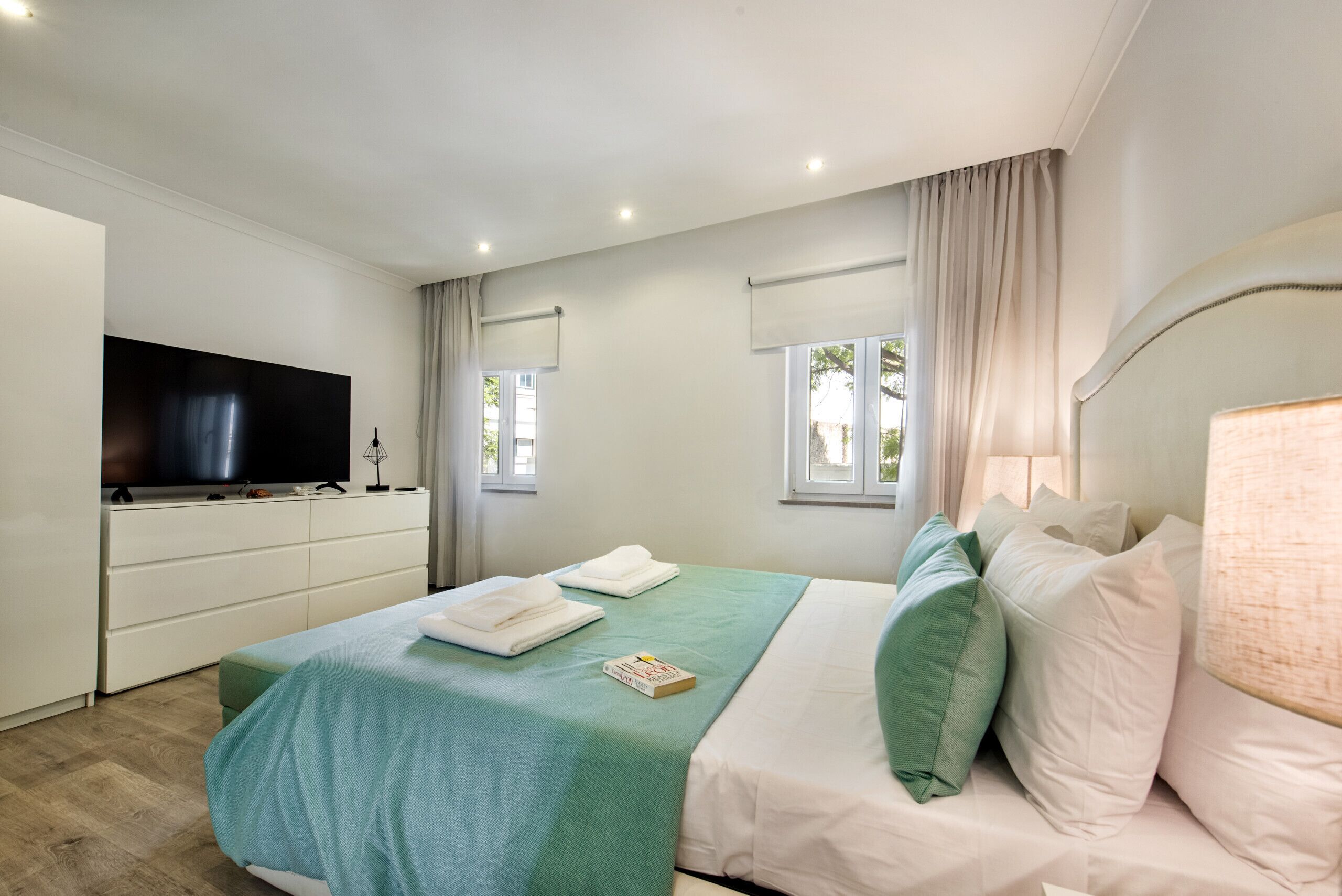A hotel room with a bed, a TV, a desk, and a window with curtains.