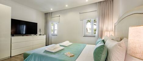 A hotel room with a bed, a TV, a desk, and a window with curtains.