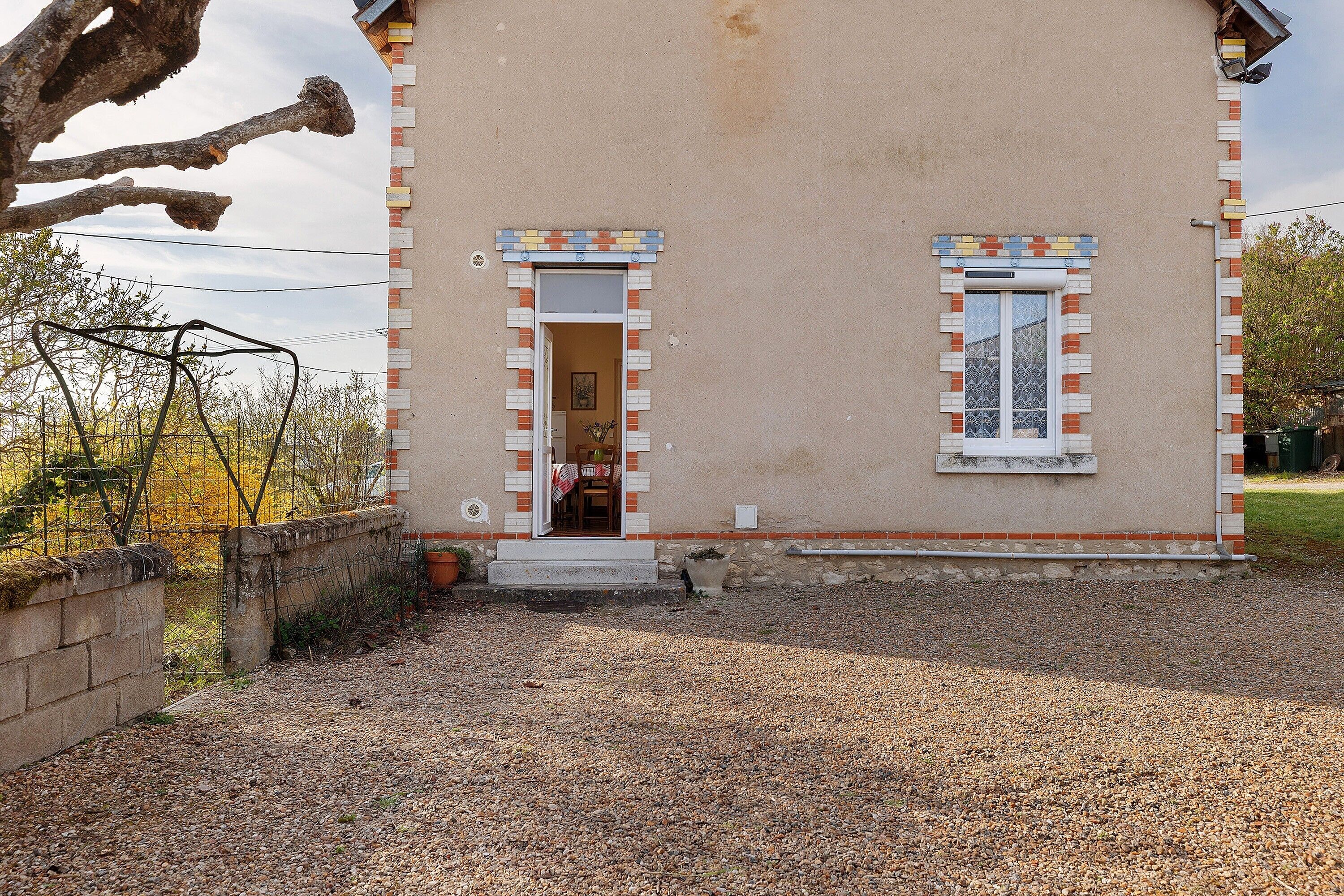 A building with a gravel driveway, a small porch, and a window with a decorative brick border.