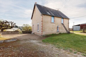 A single-story building with a sloped roof, a small window with a blue shutter, and a ladder leading to the roof.