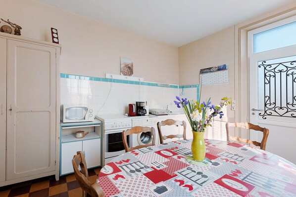 A kitchen with a microwave, stove, and cabinets, a dining table with chairs, and a window with a decorative iron grille.
