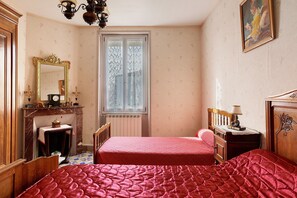 A bedroom with two beds, a wooden dresser, a mirror, a fireplace, and a window with lace curtains.
